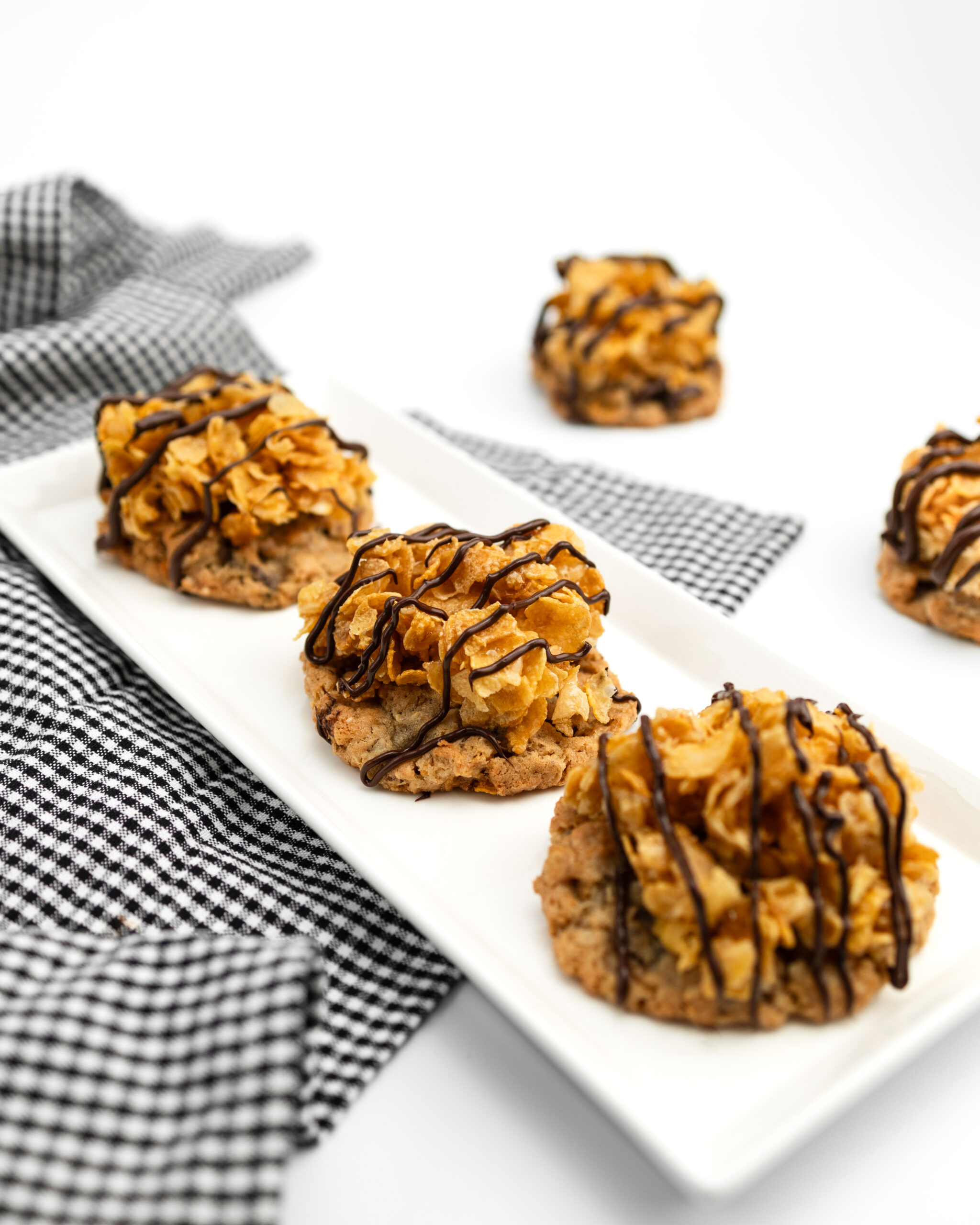 3 cookie on long white plate with cookies in background and a black and white gingham dish towel